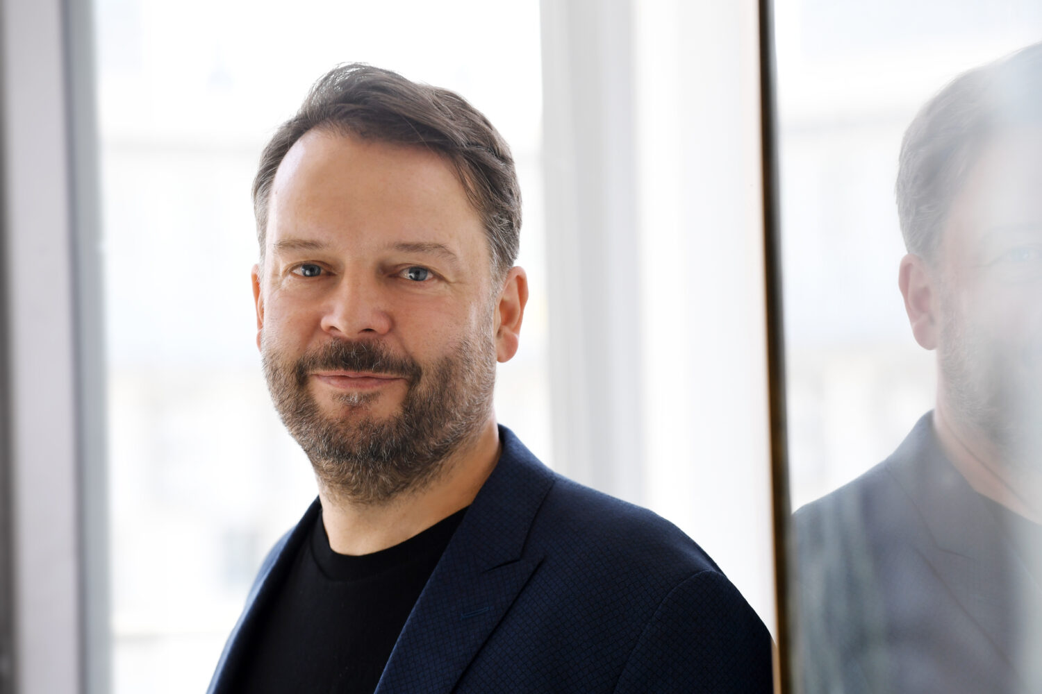 Ein Porträt von Michael Knobloch, dem Leiter der Verbraucherzentrale. Er hat einen Vollbart, braune Haare und blaue Augen. Auf dem Foto trägt er ein schwarzes T-Shirt mit einem dunkelblauen Jackett darüber.