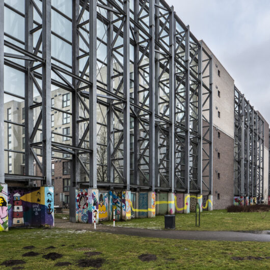 Futuristisch aussehendes Stahlkonstrukt vor einem Mehrfamilienhaus.