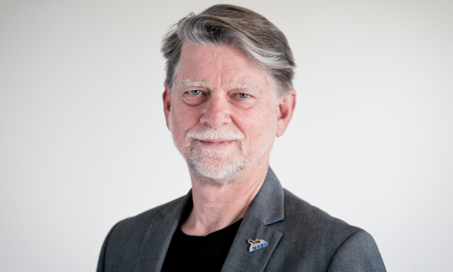 Älterer Mann im Anzug mit grauem Haar.