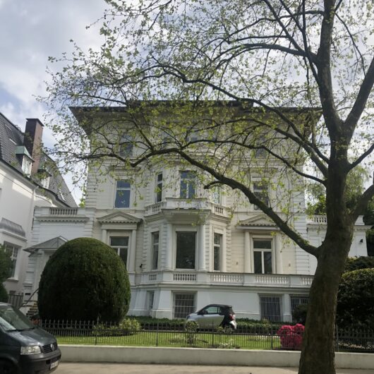 Weiße Villa an einer Straße mit Bäumen.