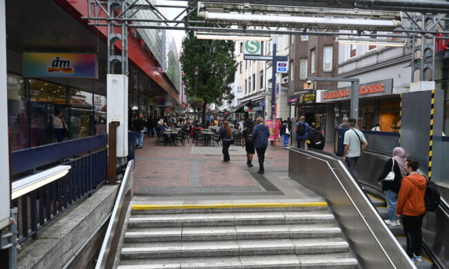 Rolltreppe und Blick in eine Einkaufsstraße mit Fußgängerzone.