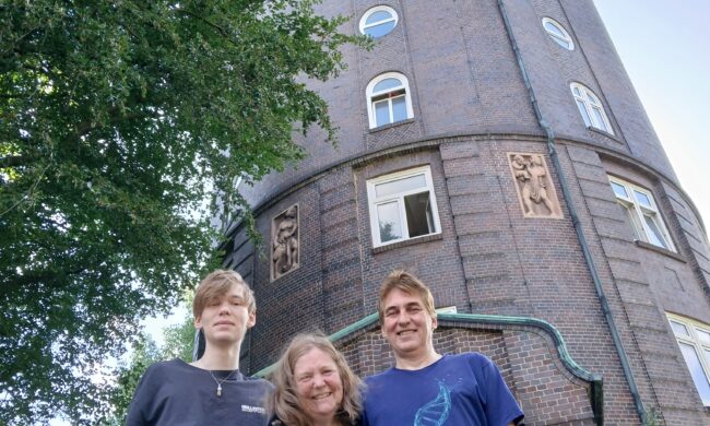 Drei Menschen stehen vor einem Wasserturm.