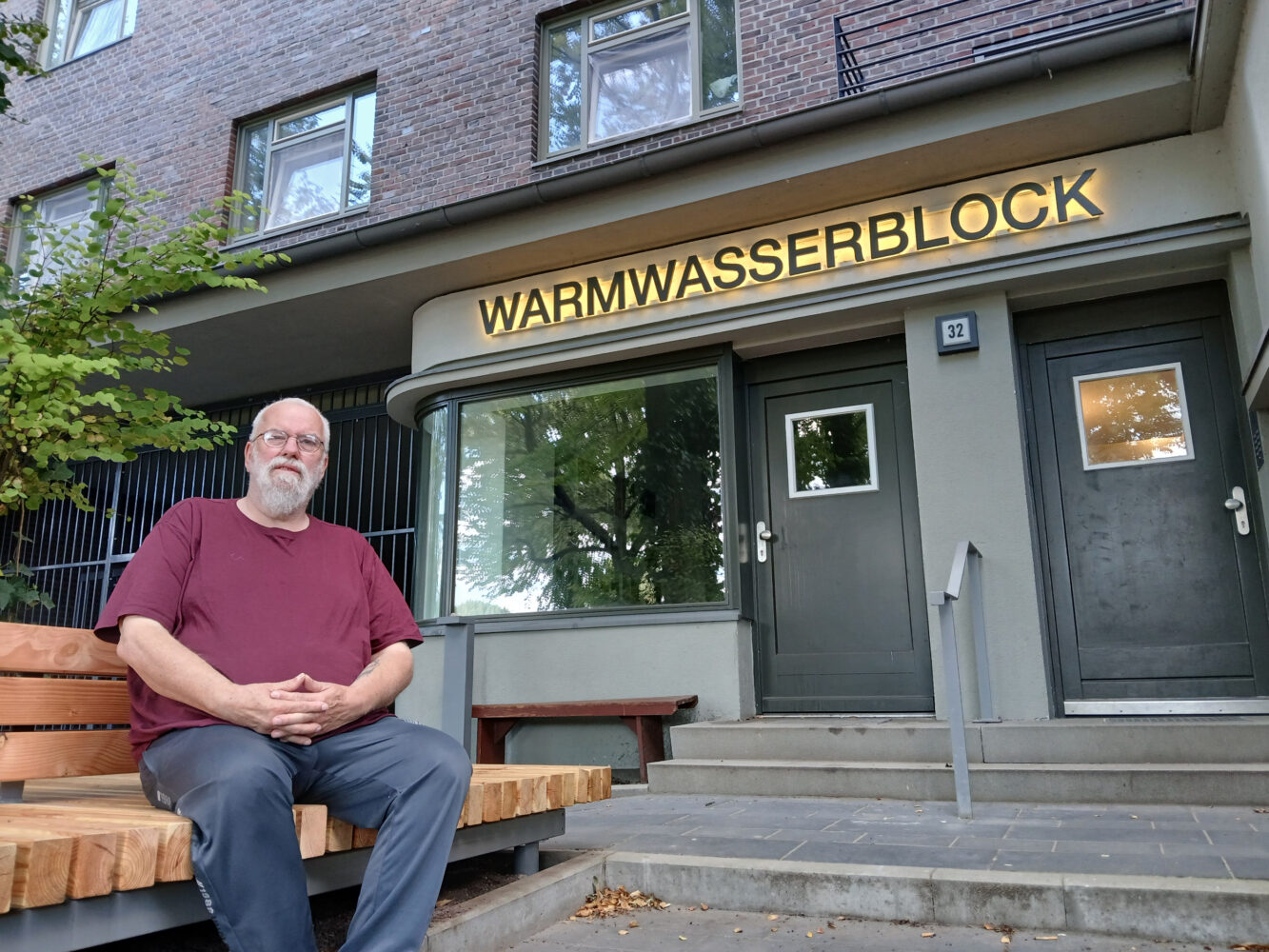 Mann sitzt vor Hauseingang übder dem Warmwasserblock steht.